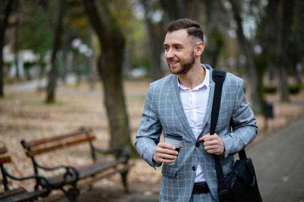 Businessman in hipster style holding takeaway coffee. Drinking his cup first thing in morning. Bearded man enjoying morning coffee. Business man with paper cup walking in city. stock photo