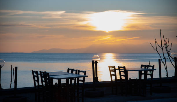 Silhouettes of tables and chairs at the cafeteria by the sea during sunset.