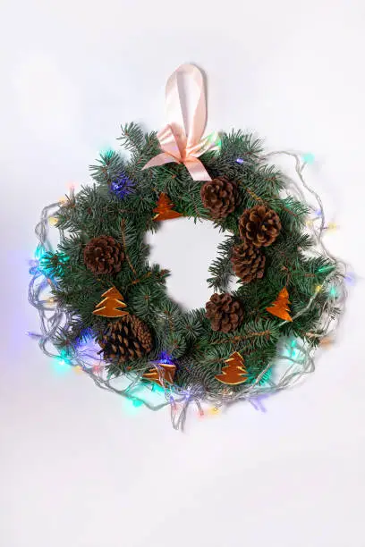 Christmas wreath flatlay. Green spruce branches decorated with orange zest, lights, pine cones and ribbon bow on white background,festive style.New Year 2020 concept.Hand made eco-friendly decorations