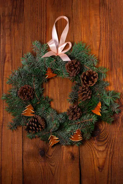 Christmas wreath flatlay. Green spruce branches decorated with orange zest, lights, pine cones and ribbon bow on wooden background,rustic style.New Year 2020 concept.Hand made eco-friendly decorations