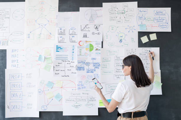 istock Back view of young elegant female broker with smartphone explaining charts 1193161625