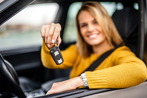 Young woman sitting in her car and holding car key.