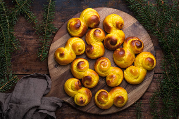 Freshly baked homemade Swedish traditional saffron buns Freshly baked homemade Swedish traditional s-shaped saffron buns, also known as lussebullar or saffransbröd. Seen from above flat lay on a dark wooden table surrounded by spruce branches. sweet bun stock pictures, royalty-free photos & images