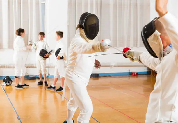 Portrait of kids and adults fencers with coaches engaged in fencing in training room