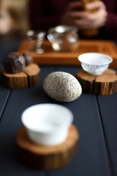 Wabi sabi concept. White stone and blurred empty tea cups on black table at tea ceremony closeup