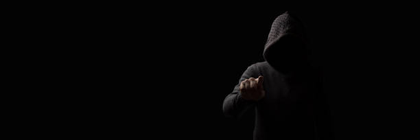 istock Faceless man in a hood with points a finger at the viewer on a dark background. Concept Threats and Terror 1193174877