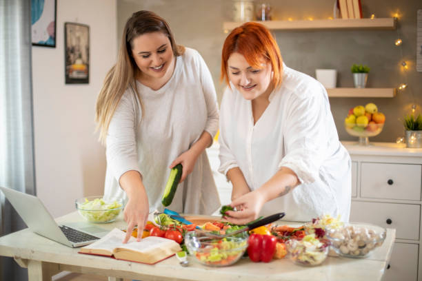 junge lächelnde plus-size-frauen bereiten salat. - fett nährstoff stock-fotos und bilder