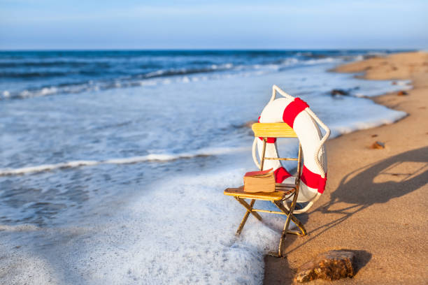 Vintage vacation scene miniature garden chair at beach shore wave, decorated by nostalgic life buoy and book (copy space)