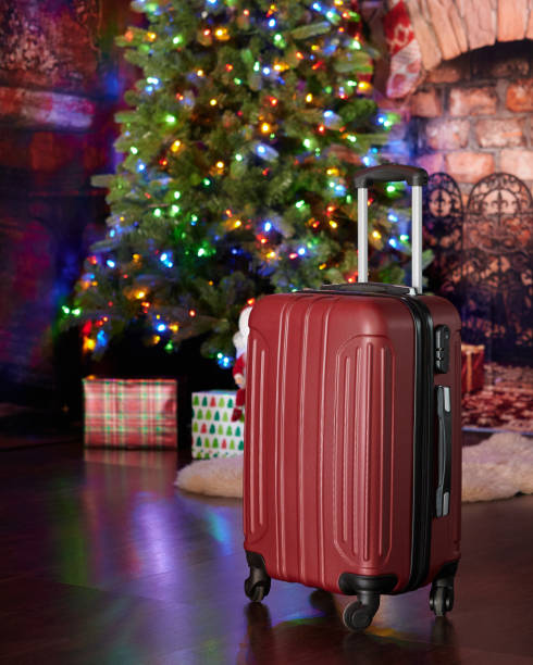 Red luggage in a Christmas decorated room with a tree , lights, gifts , fireplace, white rug stock photo