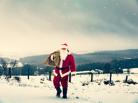 Happy Christmas holiday! Santa Claus with presents walking along a magical winter landscape. Provincial view of the countryside.