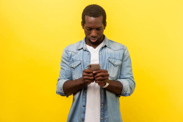 istock Portrait of serious man using cellphone, typing text message or dialing number. isolated on yellow background 1193200016