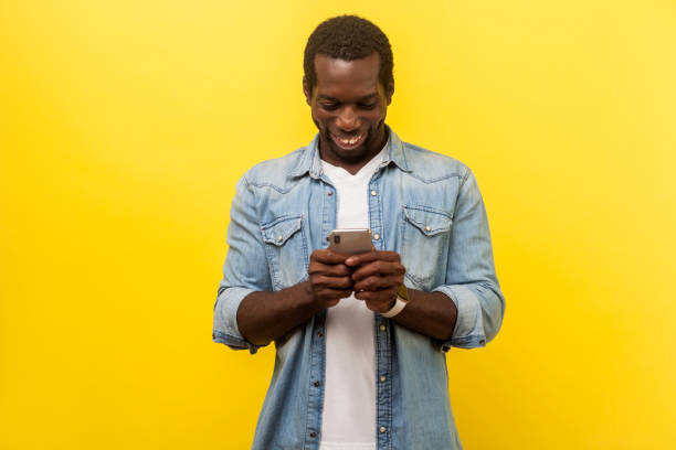 istock Portrait of happy smiley man using cellphone, typing text message or dialing number. indoor studio shot isolated on yellow background 1193200019