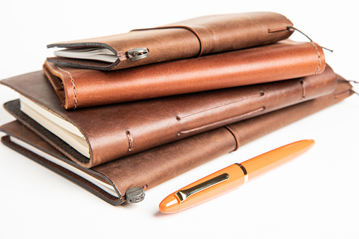 Leather-Bound Travel Journals And An Orange Fountain Pen