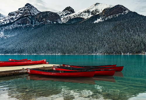 Red canoes tied to a dock on Lake Louise, Banff National Park, Alberta, Canada in winter with snow capped mountains in background