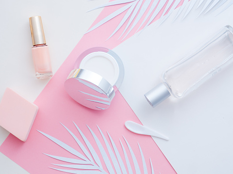 Natural cosmetics concept. White fern leaves, face, eye cream, perfume, nail polish bottle on white paper isolated on a pink color background. Flat lay, top view copy space.