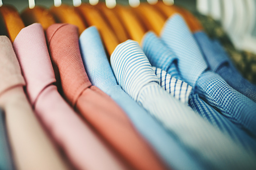 Assortment of mens shirts hanging on wooden coat hangers in a walk in closet