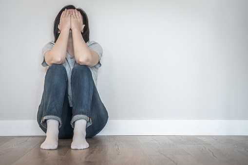 Sad woman sitting on a floor alone in empty room, despair and lonely