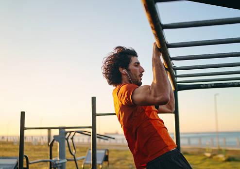 Sporty young man doing pull-ups in morning at the outdoors gym at his local park