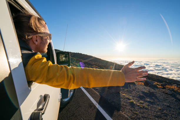 istock Young man inside car arms outstretched at sunset above clouds 1193235125