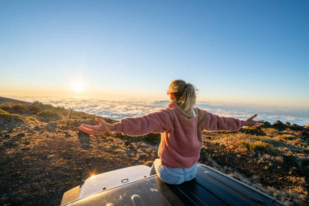 młoda kobieta siedząca na ramionach samochodu otwarta o zachodzie słońca nad chmurami - haleakala national park maui nature volcano zdjęcia i obrazy z banku zdjęć