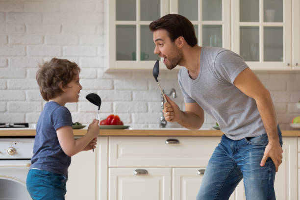 Happy father and little son playing, having fun in kitchen Happy father and little son playing funny game, having fun in kitchen, holding soup ladles as microphones, singing and dancing, dad and adorable boy child enjoying weekend at home together father housework stock pictures, royalty-free photos & images