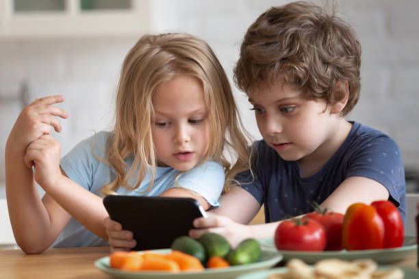 menina e menino curiosos que usam o telefone na cozinha - little boys breakfast caucasian child - fotografias e filmes do acervo