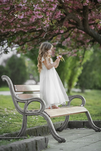 A child in a white preschool dress on the green grass in a public Park wearing a white dress.