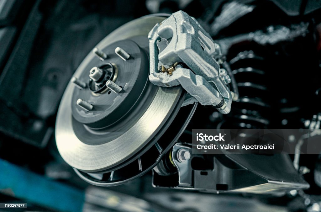 Handsome mechanic in uniform. Disc brake of the vehicle for repair, in process of new tire replacement. Car brake repairing in garage.Suspension of car for maintenance brakes and shock absorber systems.Close up. Brake Stock Photo