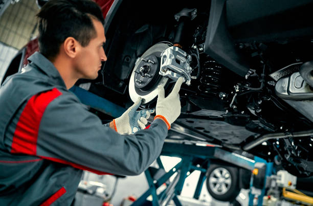 Handsome mechanic in uniform. Car mechanic worker repairing suspension of lifted automobile at auto repair garage shop station brake stock pictures, royalty-free photos & images