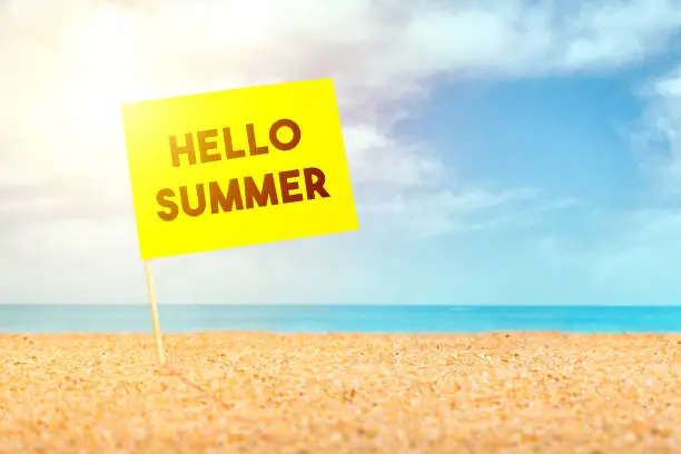 Photo of Post it with hello summer words, it stands on the sand at the beach