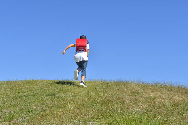 Japanese elementary school girl running in the blue sky - rear view
