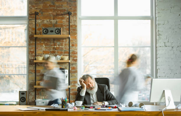 istock Nervous and tired boss at his workplace busy while people moving near blurred 1193253358