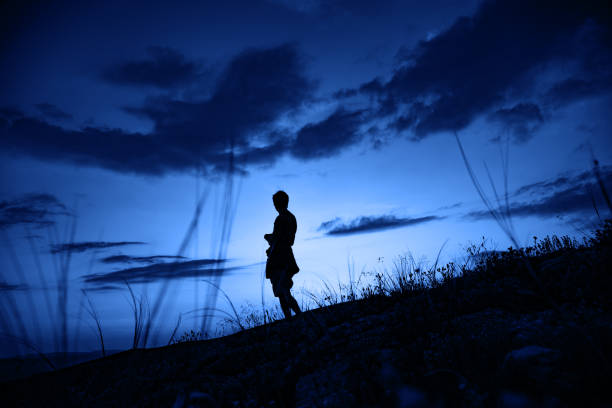 Silhouette of a men against beautiful romantic sunset sky with clouds. Outdoor travel photo. Classic blue Pantone 2020 year toned.