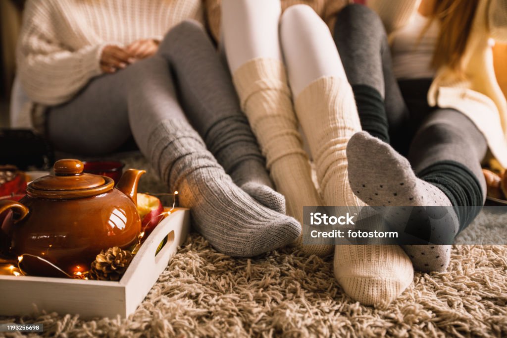 Enjoying warm tea in cozy sock on a cold autumn day Lower section of three unrecognizable young girlfriends sitting on the bedroom floor in their cozy socks and hanging out together while enjoying some warm tea on a cold autumn day. Winter Stock Photo