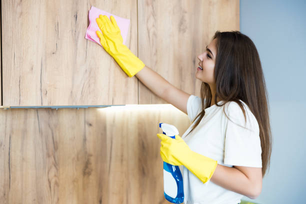 bella giovane donna sorridente con guanti gialli con spray detergente in mano che pule la polvere dall'armadietto della cucina con uno straccio che sembra felice - cleaning domestic kitchen white duster foto e immagini stock