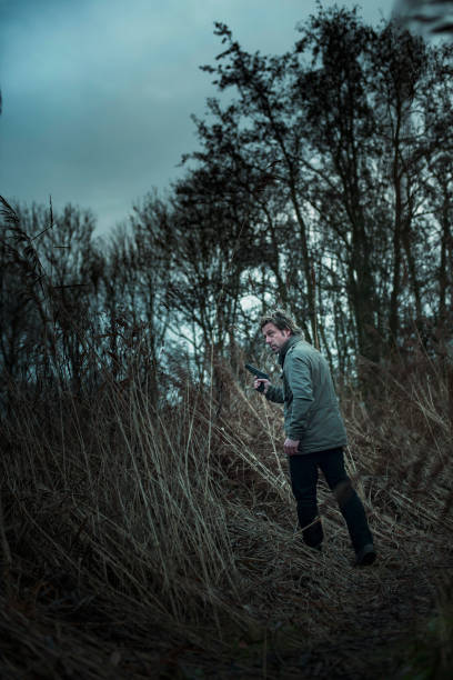 istock Man with pistol between reed on cloudy day. 1193258511