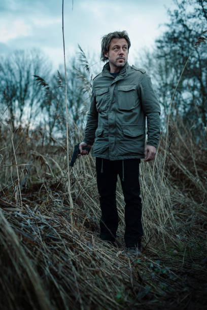 istock Man with pistol between reed on cloudy day. 1193258530