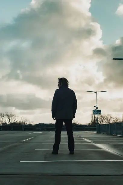 Photo of Man inspecting parking place with cloudy sky. Rear view.