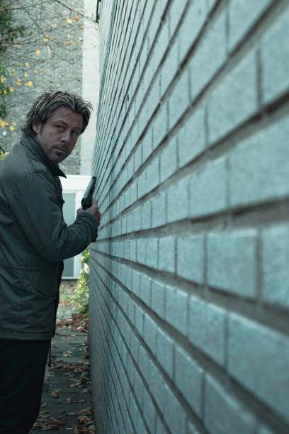 istock Man with pistol in alley along white brick wall. 1193259110