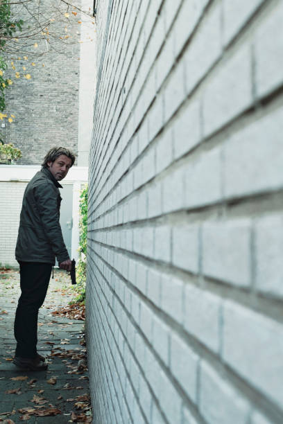istock Man with pistol in alley along white brick wall. 1193259124