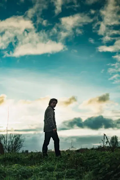 Photo of Mysterious man in rural landscape with cloudy sky at sunset.