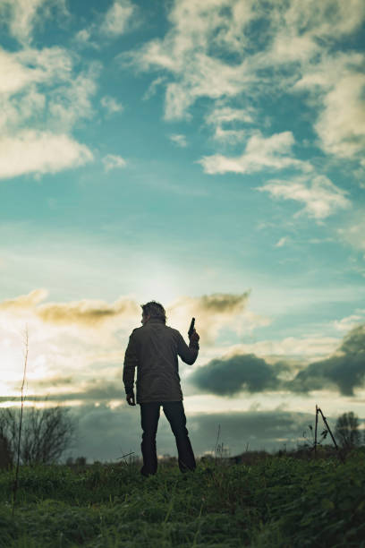 Man with handgun in countryside at sunset.