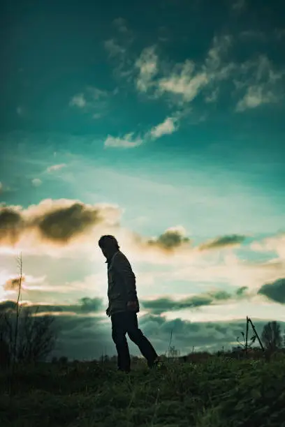 Photo of Mysterious man in rural landscape with cloudy sky at sunset.