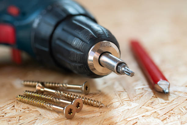 electric screwdriver, self drilling screws and carpenter pencil lying on chip board. blurred background. - drill red work tool power imagens e fotografias de stock