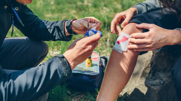 Man healing knee to woman who has been injured trekking Young man healing knee to a young woman who has been injured doing trekking man sitting with a bandage on his leg stock pictures, royalty-free photos & images