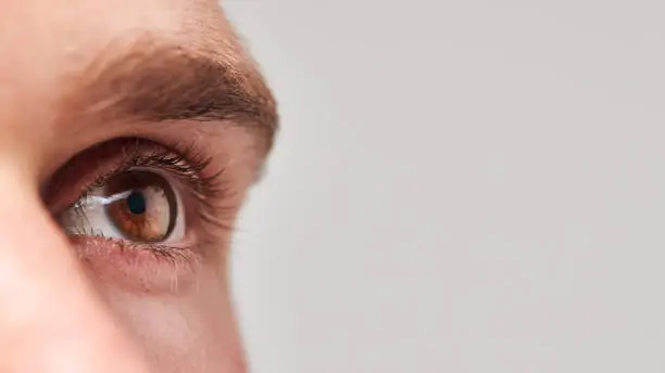 Photo of Extreme Close Up Of Eye Of Man Against White Studio Background