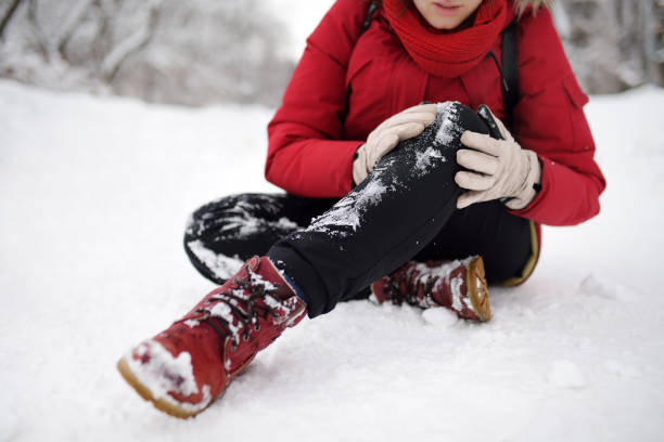 Shot of person during falling in snowy winter park. Woman slip on the icy path, fell, injury knee and sitting in the snow. stock photo
