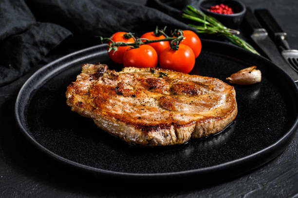 istock Roast pork steak with tomatoes. Black background. Top view 1193275320