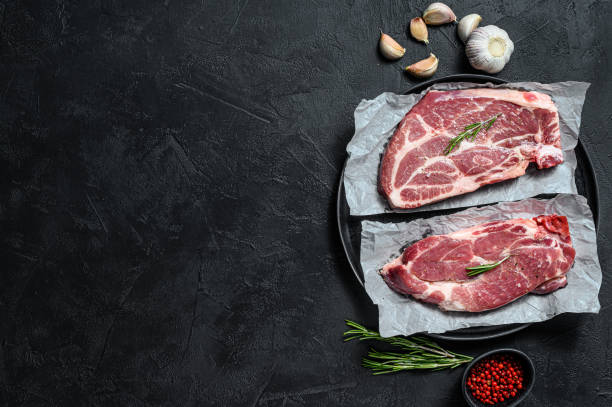 istock Raw pork steak. Marble meat on parchment paper. Black background. Top view. Space for text 1193276345