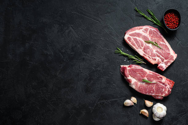 istock Raw pork steak on the bone. Grilled meat. Black background. Top view. Space for text 1193276638